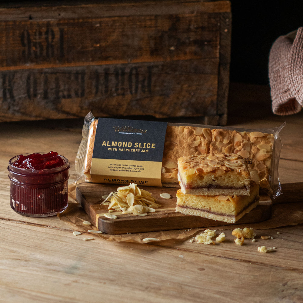 Almond Slice with Raspberry Jam, with two loose slices sat in the foreground, next to a pot of jam and flaked almonds.